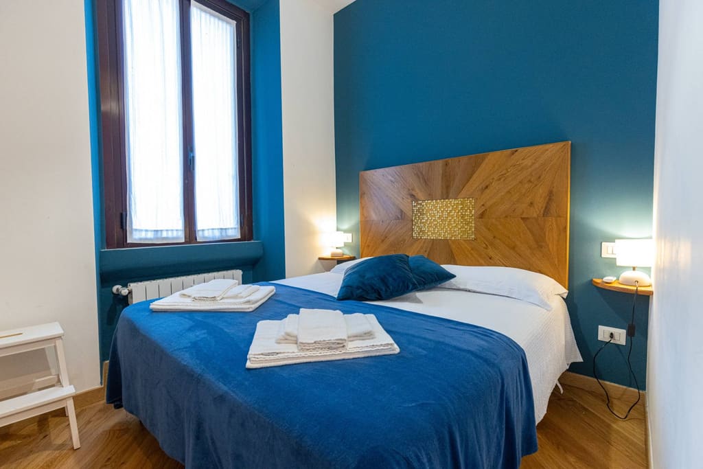 La camera con letto matrimoniale, testiera in legno e parete blu petrolio
